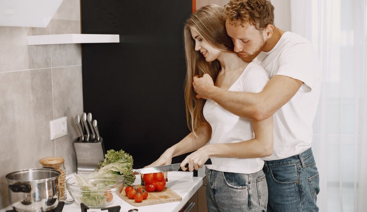 A loving couple enjoys cooking fresh vegetables together in a cozy, modern kitchen setting.