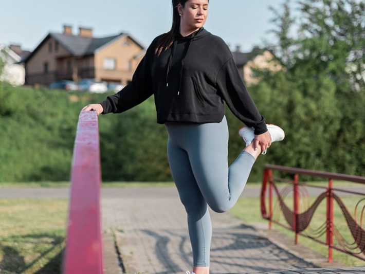 Young woman in activewear stretching on a red railing outdoors.