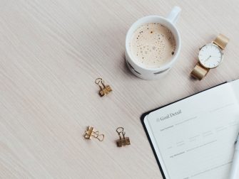 A minimalist desk arrangement featuring a coffee cup, notebook, pen, and wristwatch.