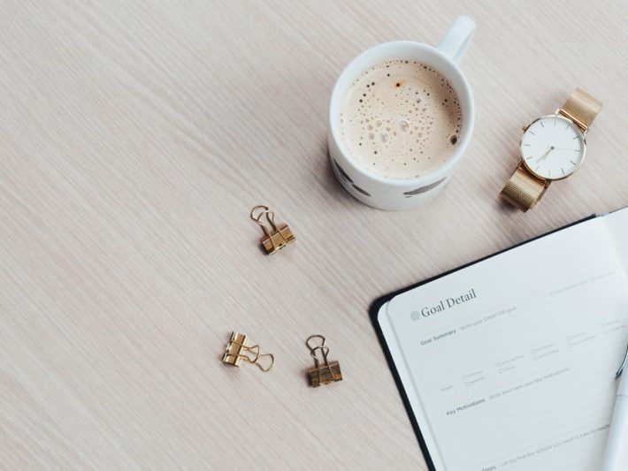 A minimalist desk arrangement featuring a coffee cup, notebook, pen, and wristwatch.